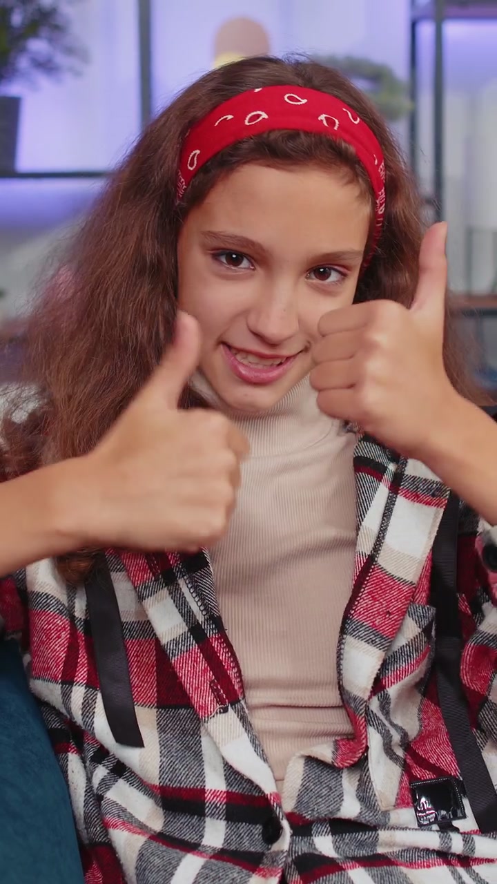 Ragazza felice che guarda con approvazione la telecamera mostrando i pollici in alto come un segno positivo di buone notizie