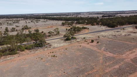 avión no tripulado volando sobre carreteras no selladas hacia una carretera sellada en un paisaje de estilo desierto