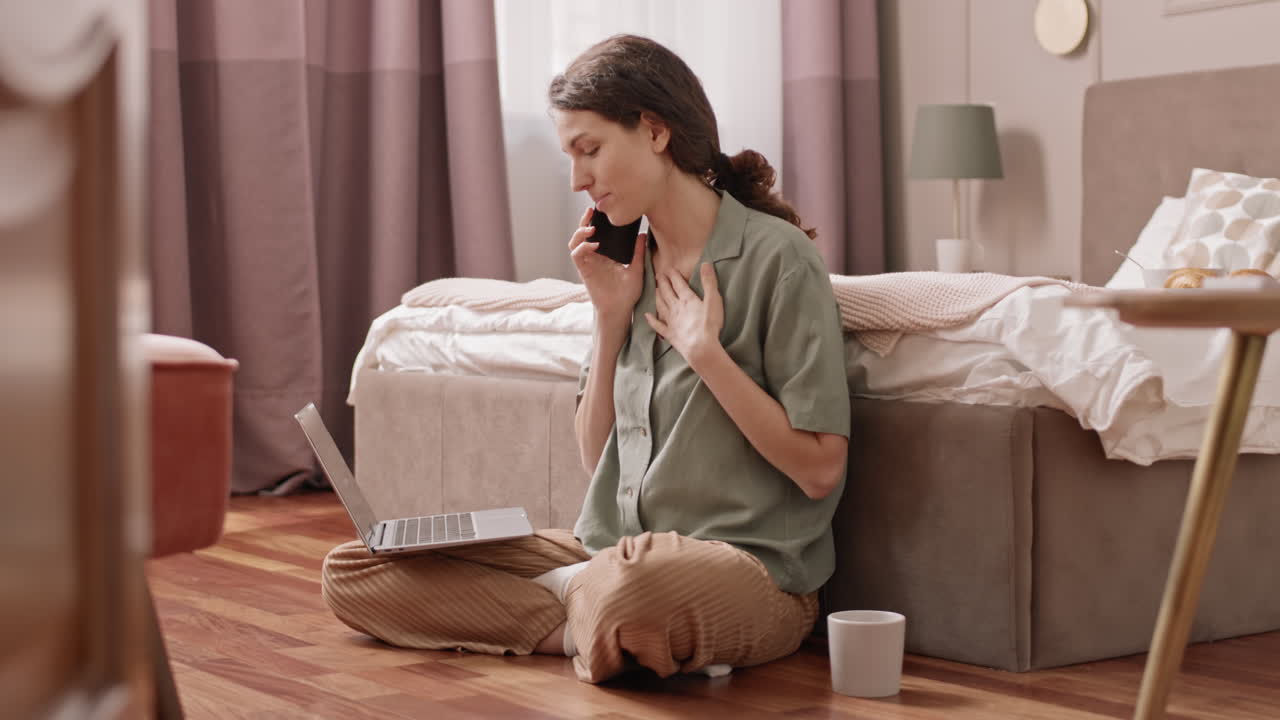 Woman using laptop and talking on the phone in bedroom
