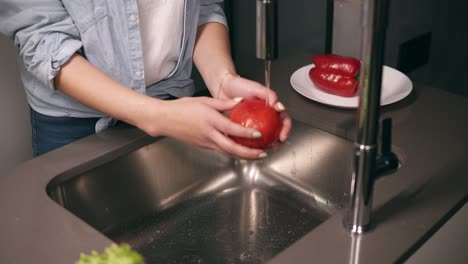 woman washing red pepper, cucumbers and tomato in kitchen and putting them on plate. homemade food concept. young woman washes