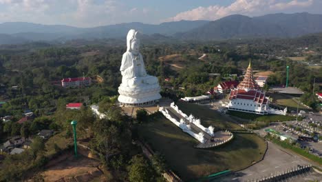 aerial drone of wat huay pla kang giant white big statue and pagoda temple with mountains and landspace in chiang rai, thailand