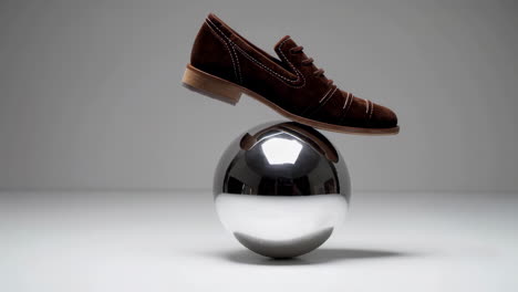 brown suede shoe balancing on a chrome sphere