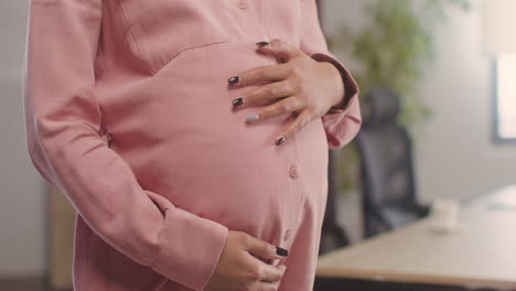 nahaufnahme der nicht erkennbaren hände der schwangeren frau, die ihren bauch streicheln