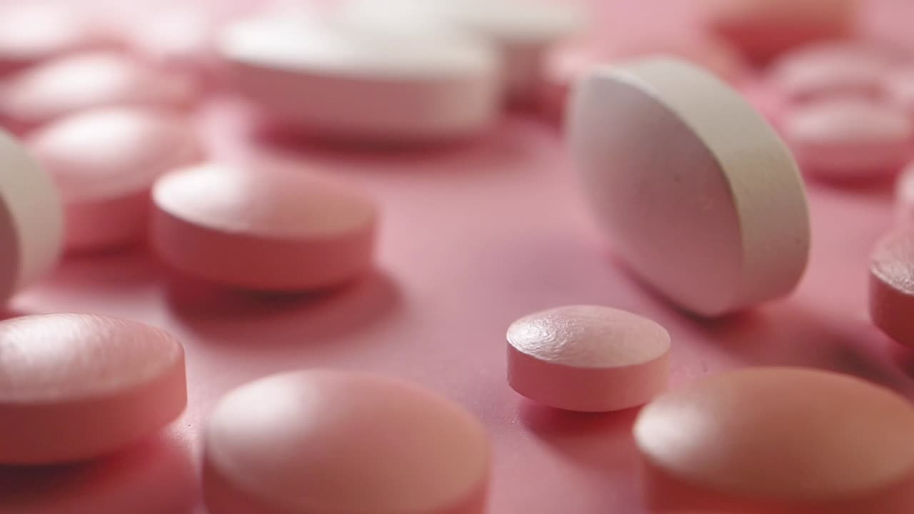 Close-up view of pink and white medical pills on a pink background