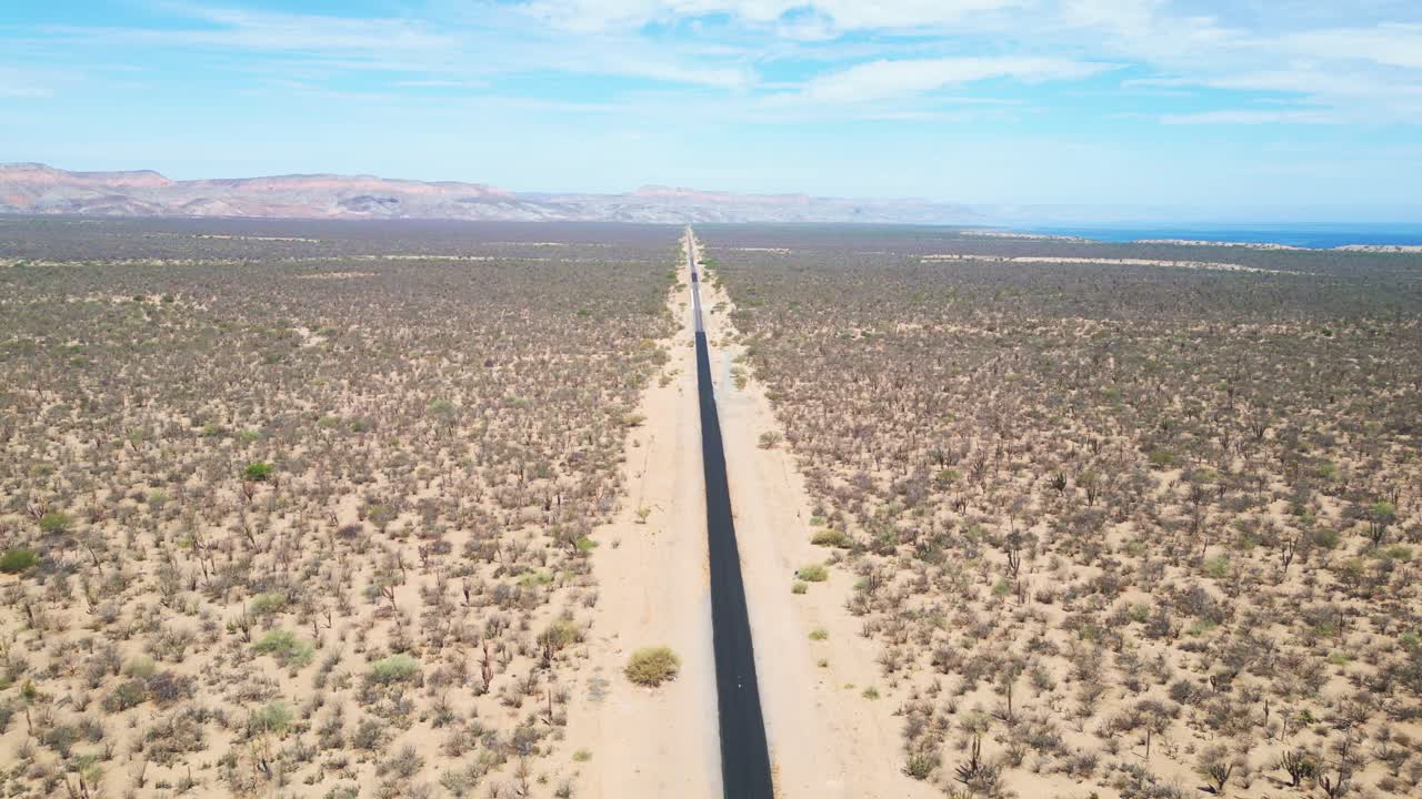 An empty desert road stretching through la paz, mexico, surrounded by dry landscape, aerial view