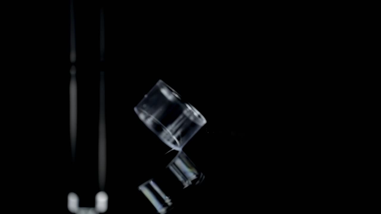 Sleek clear plastic cap spins rolling in slow motion as empty bobbin exits out of focus and out of view