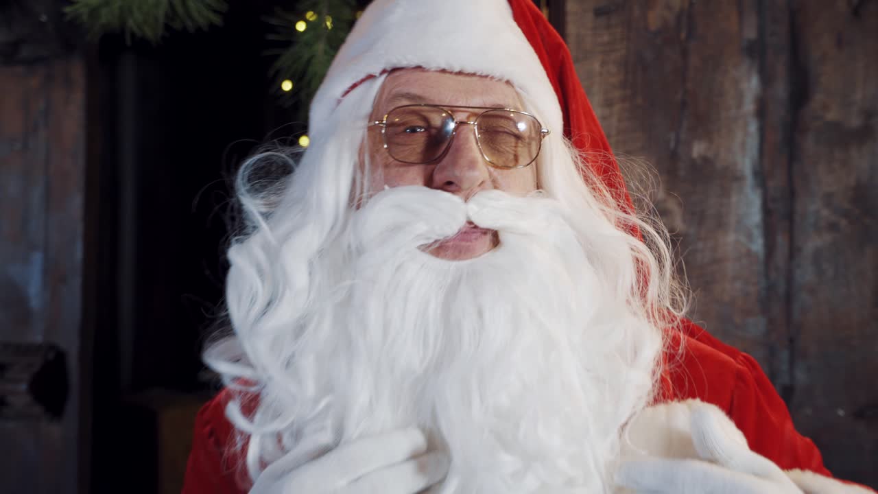 Portrait of Santa in eyeglasses looking at camera. Old Santa Claus with white beard and blinks his eyes through his glasses. Close-up.