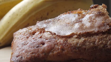 right pan view of banana bread cut in half on a wooden board with a bananas in the back.
