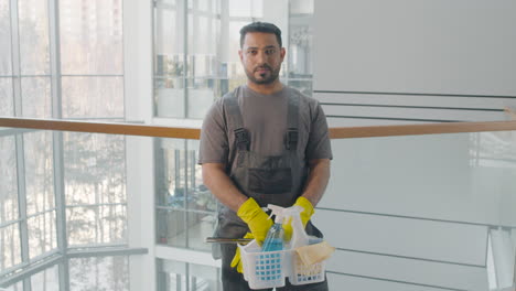 retrato de un limpiador árabe posando y mirando la cámara mientras sostiene productos de limpieza dentro de un edificio de oficinas 1