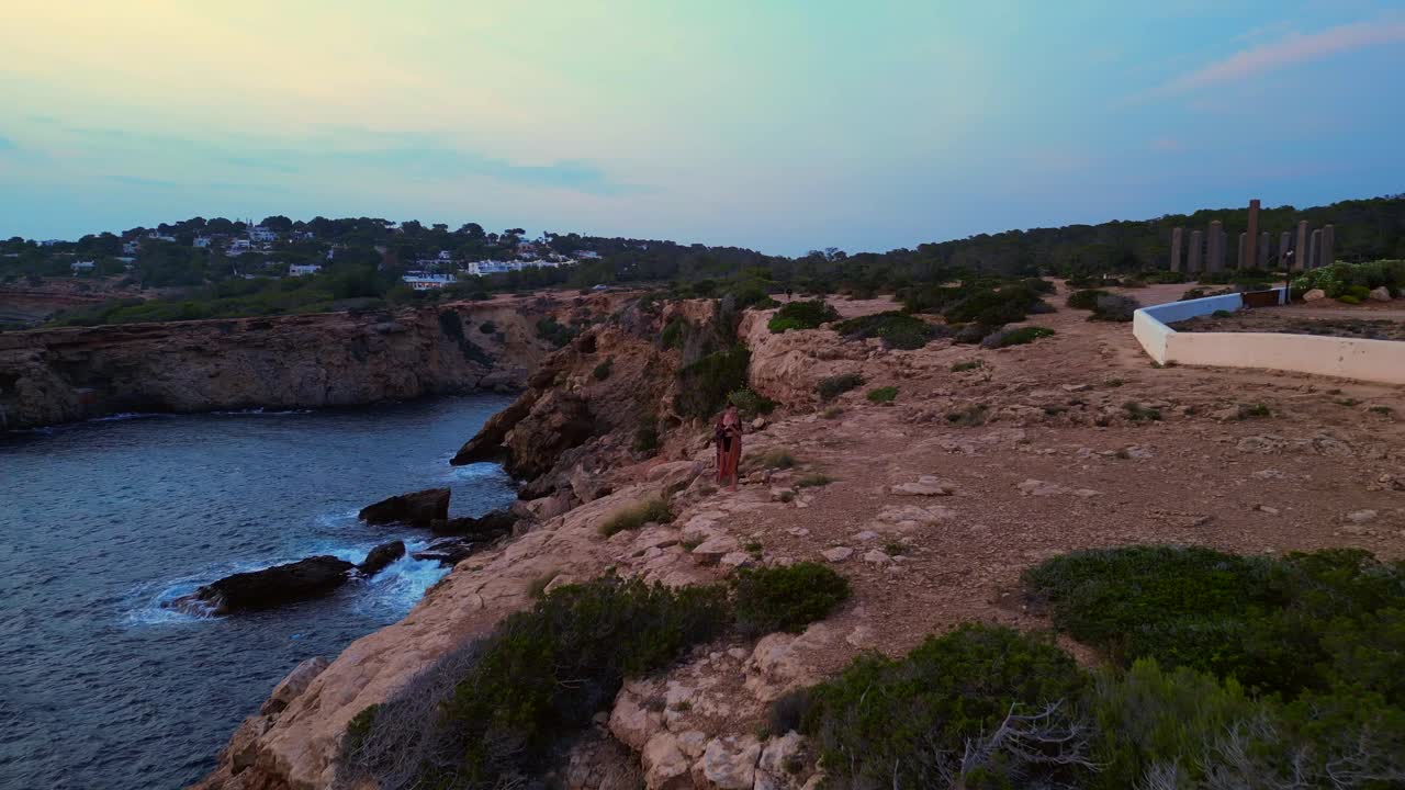 Donna che balla esprimendo libertà e movimento in riva al mare in una bellissima destinazione di viaggio, Cala Llentia, Ibiza. Vista aerea perfetta, volo, avanzamento, drone