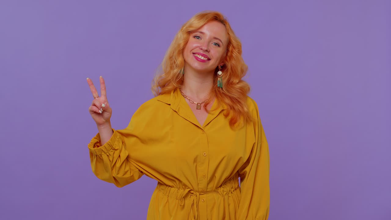 Bella ragazza elegante e sorridente che fa il segno della vittoria, sperando nel successo e nella vittoria.