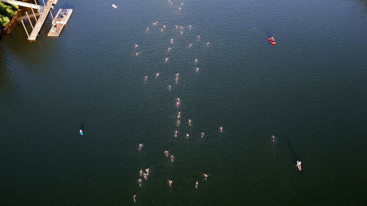 Swimmers begin the Ironman Chattanooga swim leg, creating ripples across the Tennessee River as kayakers monitor their progress from above