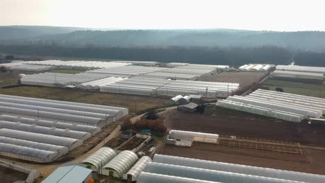 an aerial shot rising above a field with industrial greenhouses