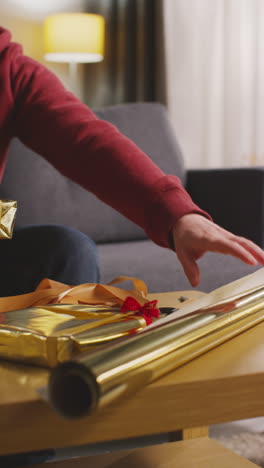 vertical video of man wrapping gift or present on table at home with scissors sticky tape and ribbon 1