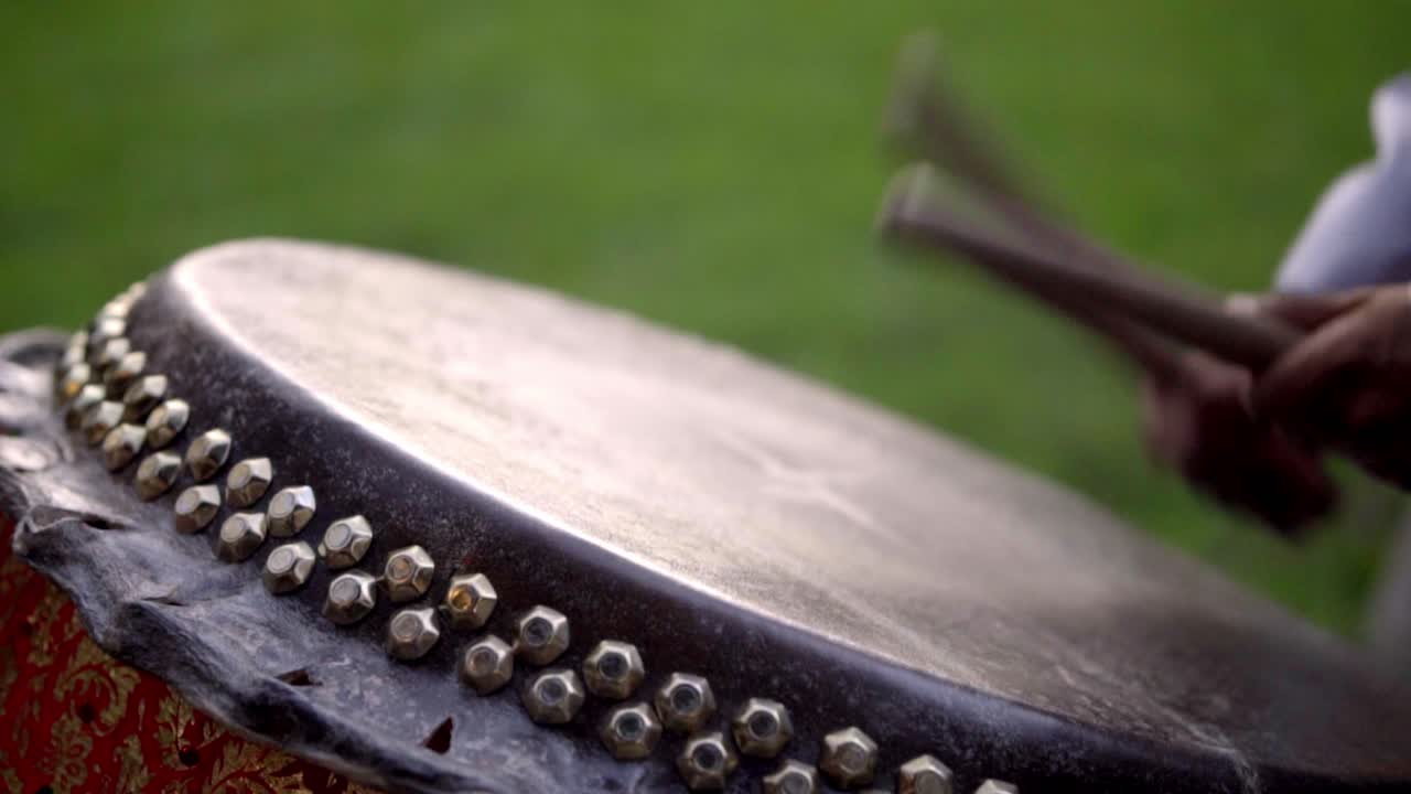 Person drumming energetically in an outdoor setting, creating music