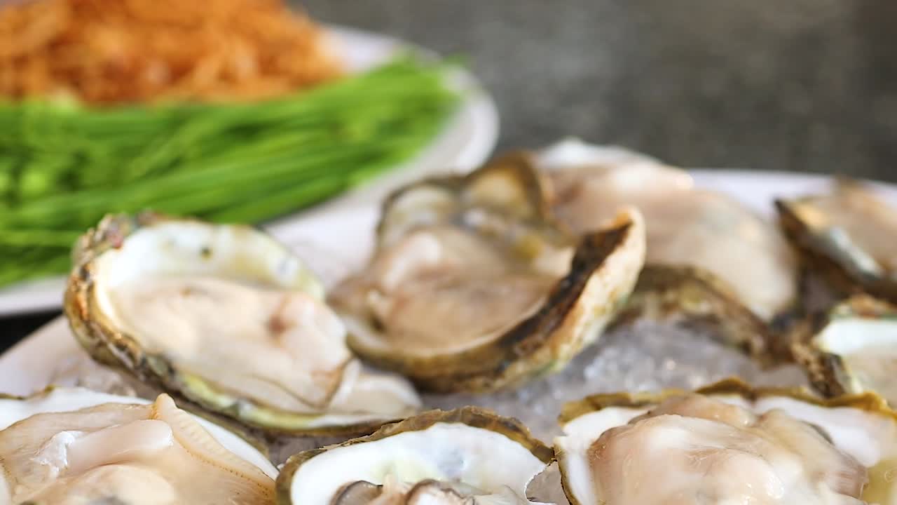 Close-up of fresh oysters on ice, accompanied by green vegetables and crispy toppings.