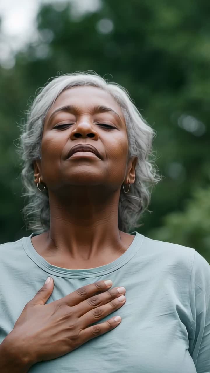 Video verticale: Anziana donna che respira dopo aver chiuso gli occhi, mano sul petto in un parco per la calma, con maglietta.