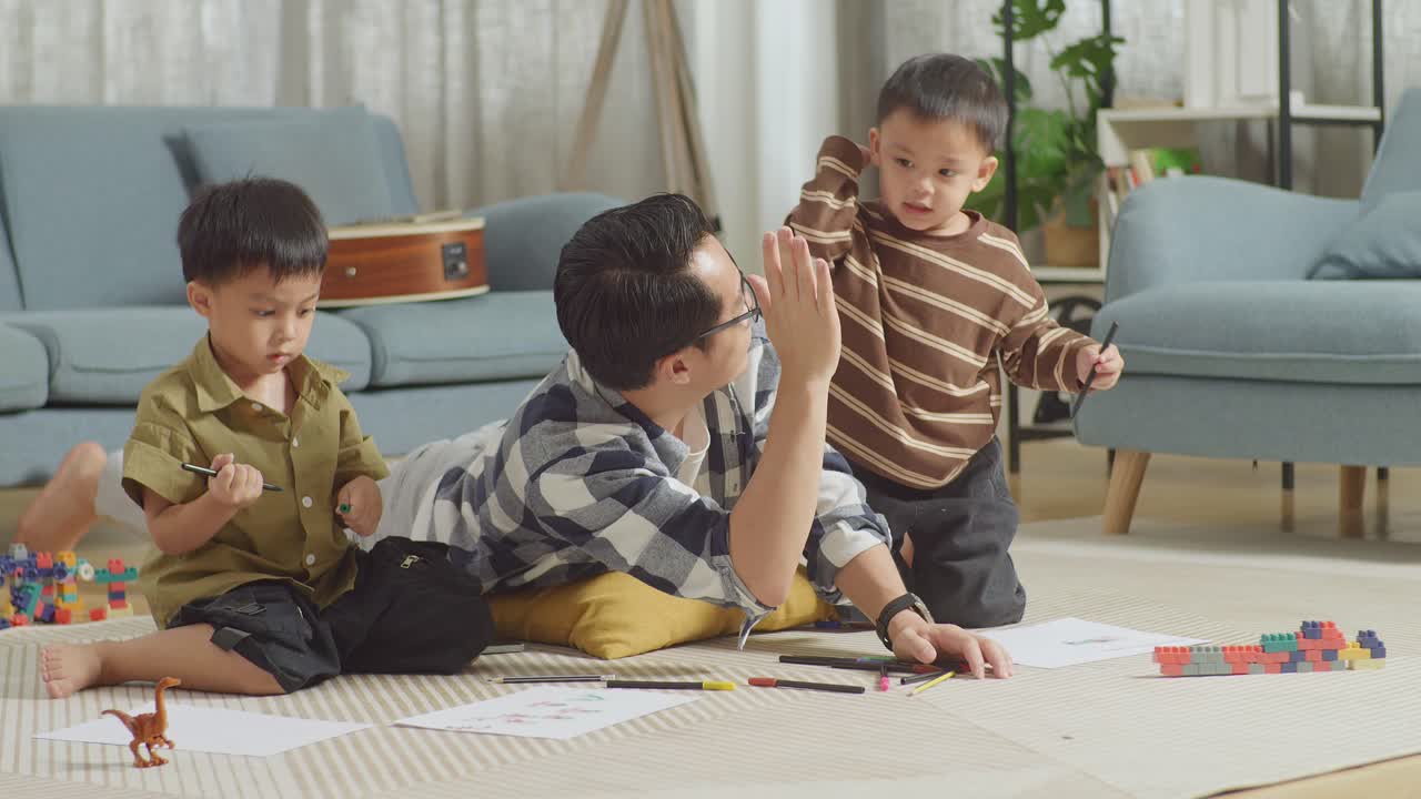 아시안 아버지와 아들의 몸이 가득 차있는 방에서 바닥에 플라스틱 장난감 벽돌을 가지고 집에서 함께 그림을 그리고 손을 치고 성공을 축하합니다.
