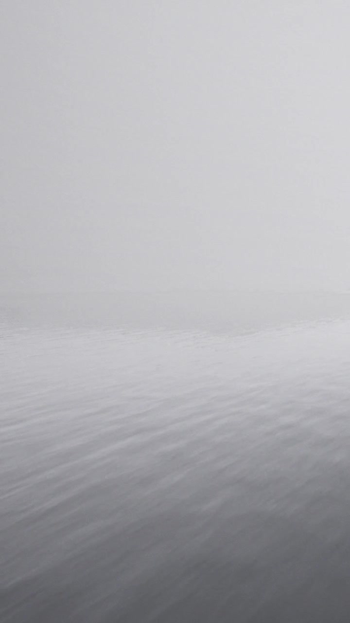 Fog surrounds calm water during early morning hours in a quiet location