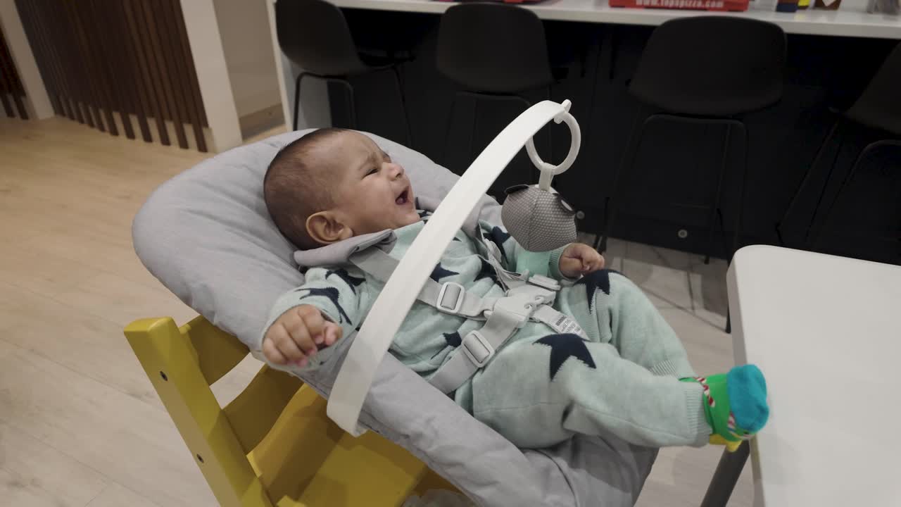 Adorable 4-month-old bubbling with joy in a baby chair, gleefully jiggling and smiling