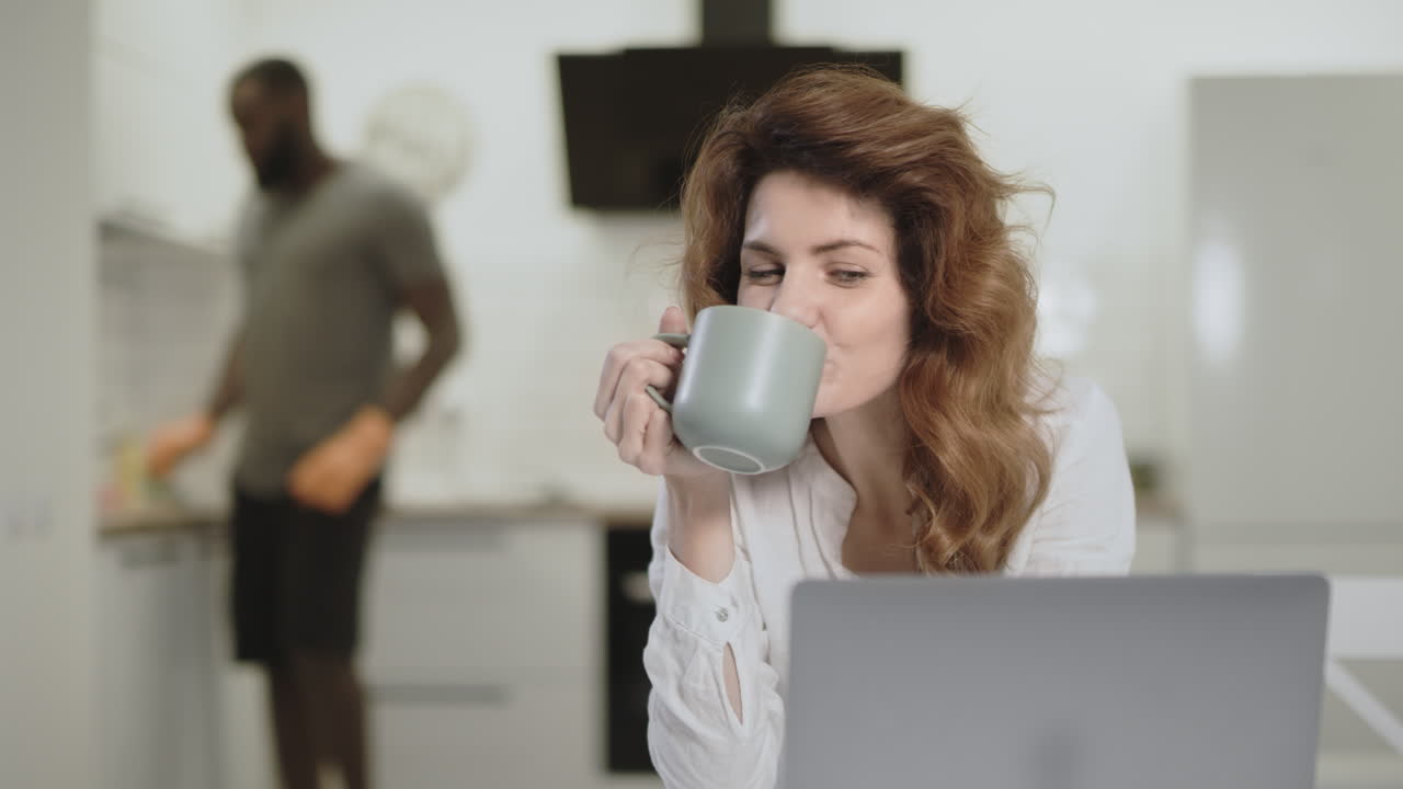 미소 짓는 여자 가 오픈 주방 에서 컴퓨터 에서 재미 있는 뉴스 를 보고 있다