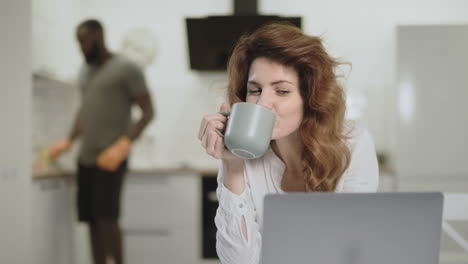 Mujer-Sonriente-Viendo-Noticias-Divertidas-En-La-Computadora-En-La-Cocina-Abierta