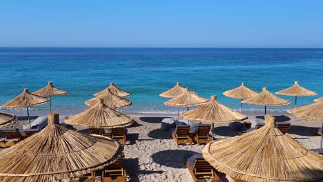 blue turquoise sea and clear sky in a sunny summer vacation day on quiet beach with sunchairs and umbrellas, ionian coastline of albania