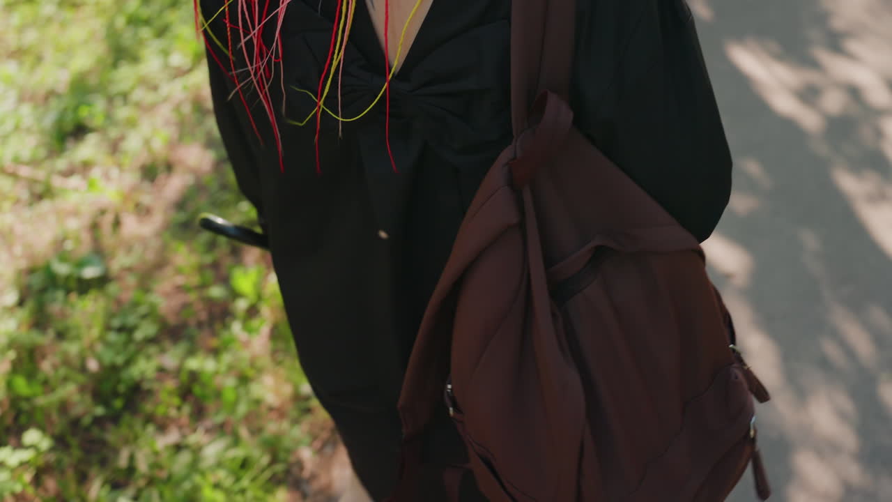 Женщина идет по улице; девушка с неоновыми косами целеустремленно идет по тенистой городской тропе; модная женщина с рюкзаком и зонтом уверенно шагает по утопающей в зелени городской дорожке в полдень