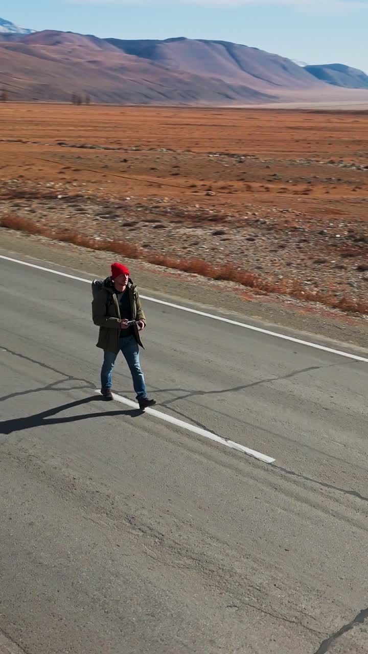 Caminhante com Mochila Percorre Estrada Remota em Direção às Montanhas
