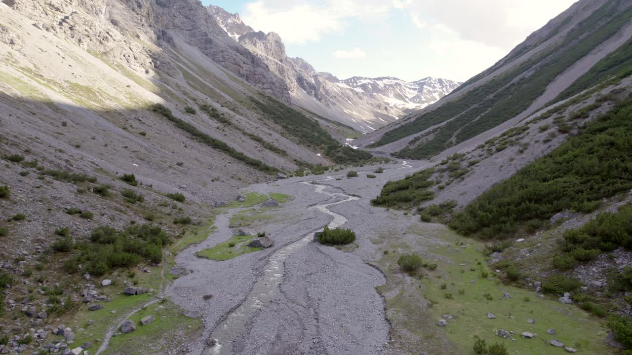 imágenes aéreas de drones girando y descendiendo lentamente en un espectacular valle glacial rodeado de montañas empinadas y pinos con parches de nieve y un río alpino en suiza
