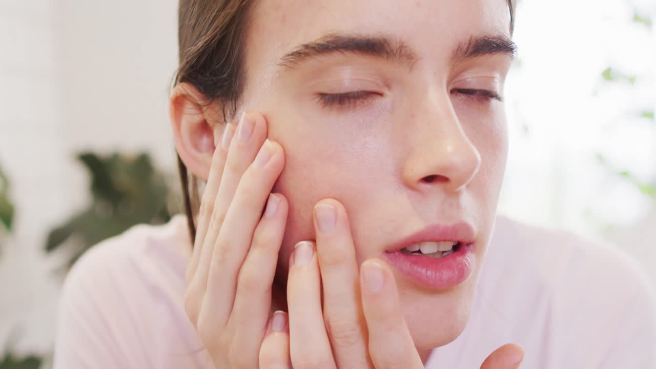 백인 비 바이너리 트랜스젠더 여성이 얼굴을 만지고 있습니다.