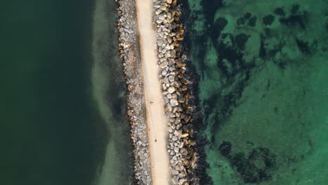 Aerial-top-down-shot-of-walking-people-along-jetty-between-clear-Pacific-Ocean-in-Fremantle,-Western-Australia-at-sunset-time