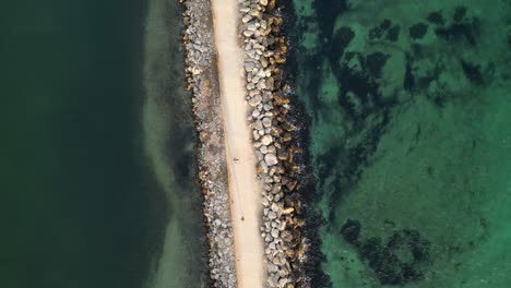 aerial top down shot of walking people along jetty between clear pacific ocean in fremantle, western australia at sunset time