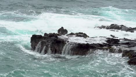 las olas del océano pacífico chocan contra rocas irregulares en la costa de kauai.