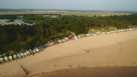 drone shot along sandy beach with beach huts and woodland behind on sunny morning in wells-next-the-sea north norfolk uk east coast