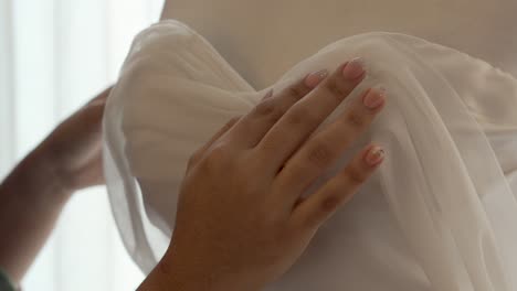las manos de la novia acarician la tela de su vestido durante la preparación de su boda