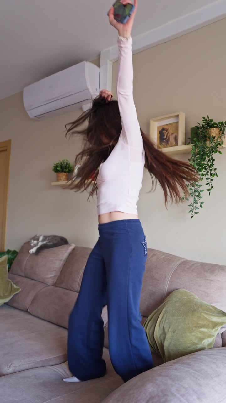 Donna giovane felice che balla energicamente sul divano a casa
