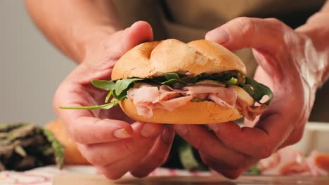 mortadella ham sandwich, traditional italian focaccia filled with thin pesto slices of mortadella, served by chef man in cafe restaurant. macro of traditional italian spanish tapas antipasti.