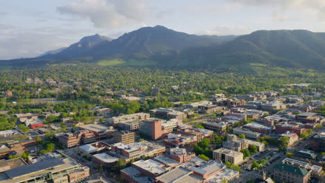 Aerial-shot-forward-of-beautiful-flatiron-mountain-vista-and-bright-green-trees-in-downtown-Boulder-Colorado-during-an-evening-sunset-with-warm-light-on-the-rocky-mountain-town-and-summer-landscape