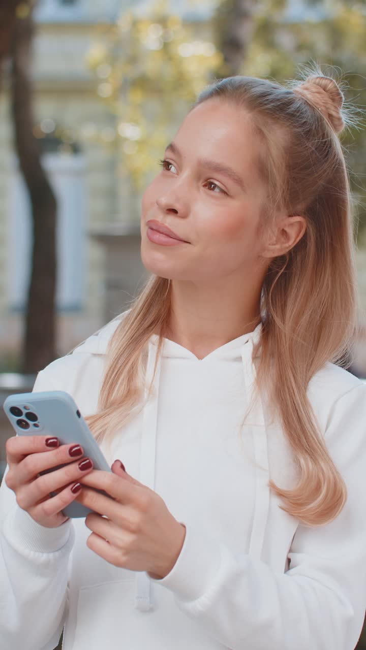 Happy caucasian woman using smartphone typing text messages browsing internet on city town street