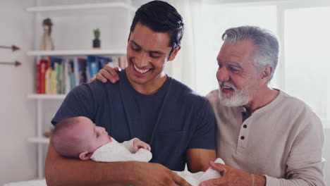 proud hispanic father holding his four month old son at home, with grandfather beside them, close up
