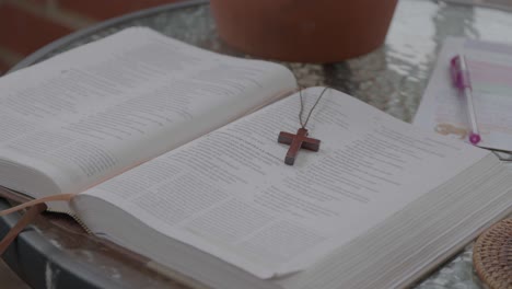 open bible with a wooden cross necklace laid on its pages, accompanied by study notes and a pen