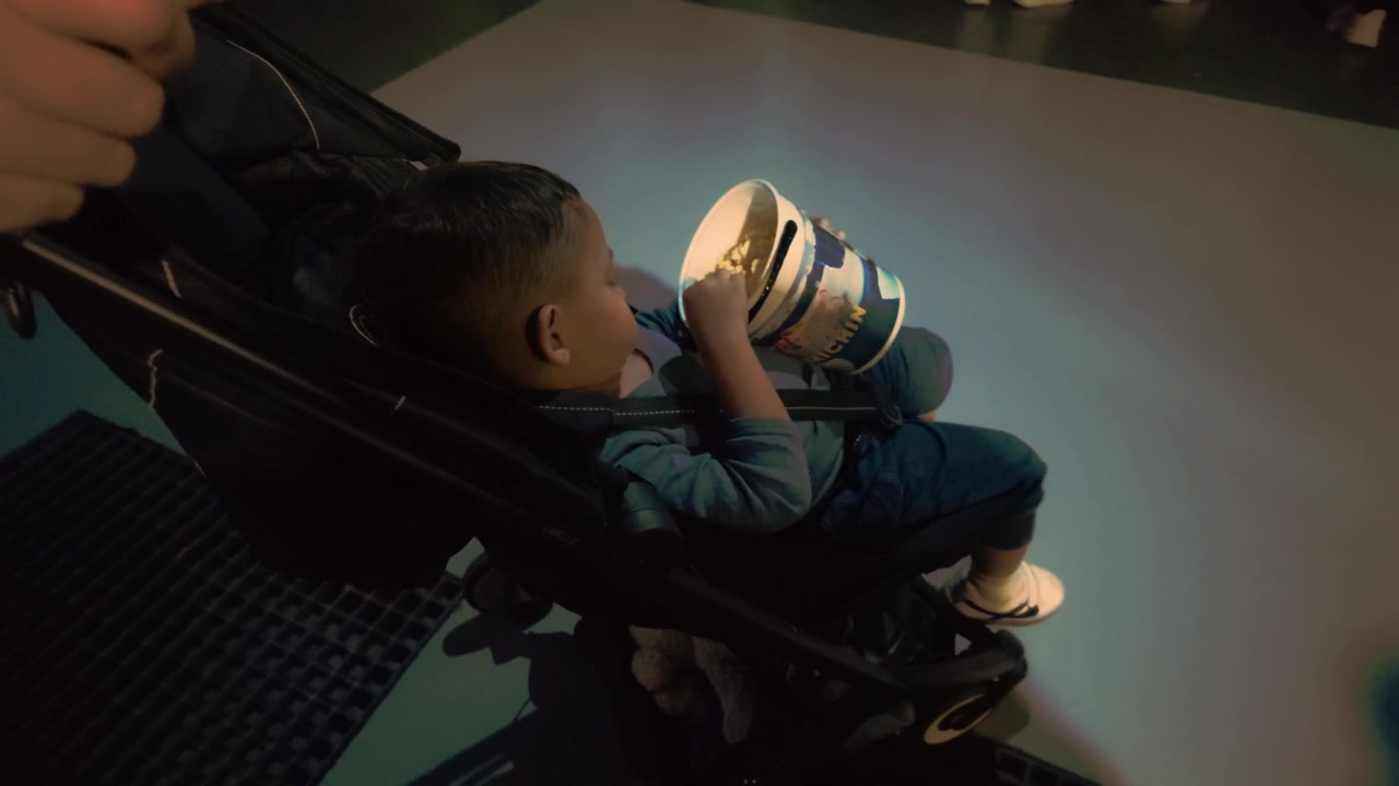 Un adorabile bambino latino di due anni mangia comodamente popcorn mentre viene spinto in passeggino dalla madre all'interno dell'Acquario Michin a Città del Messico. Ripresa dall'alto, contenuto generato dall'utente