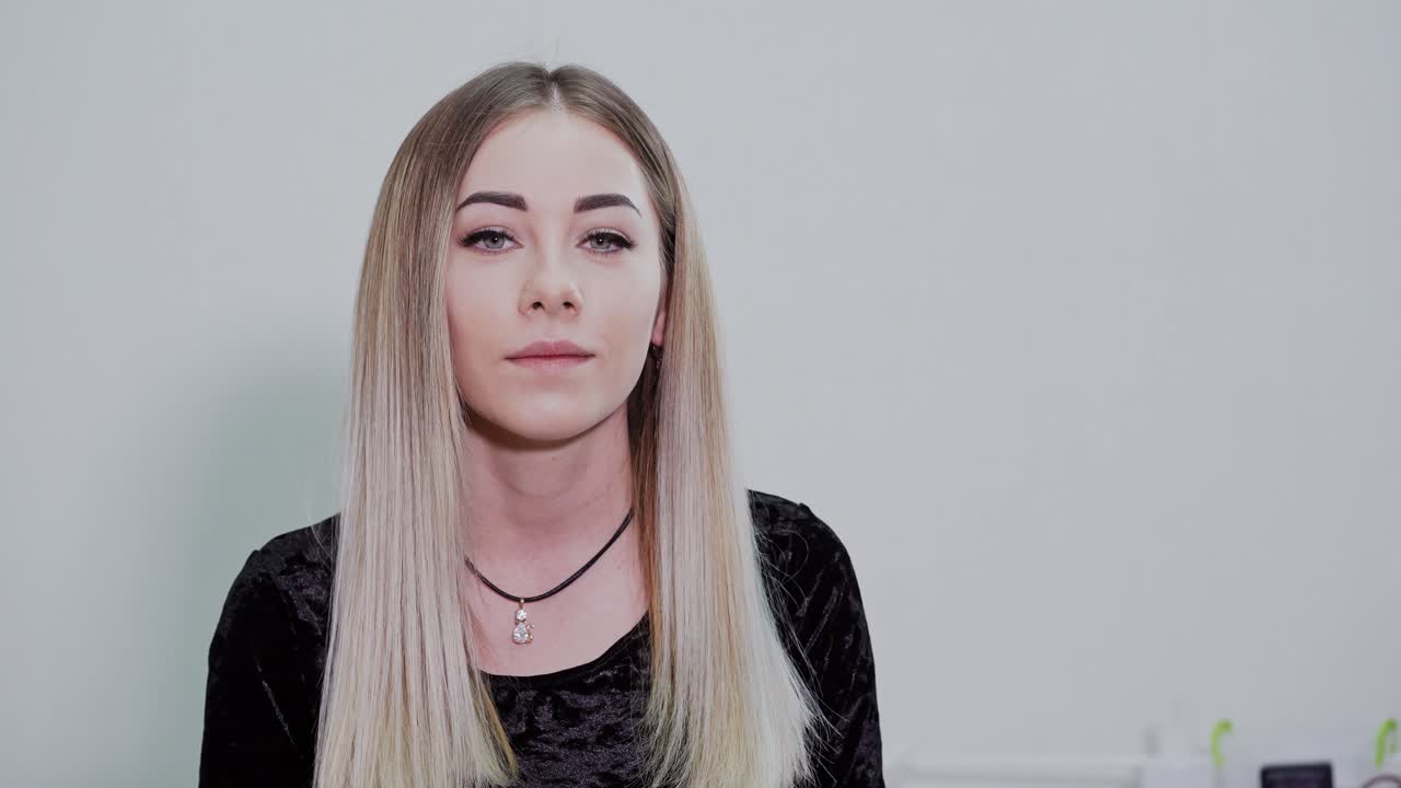 Lovely girl in studio. Portrait of a blonde girl sitting on light background and posing on camera. Natural facial features of a young woman.