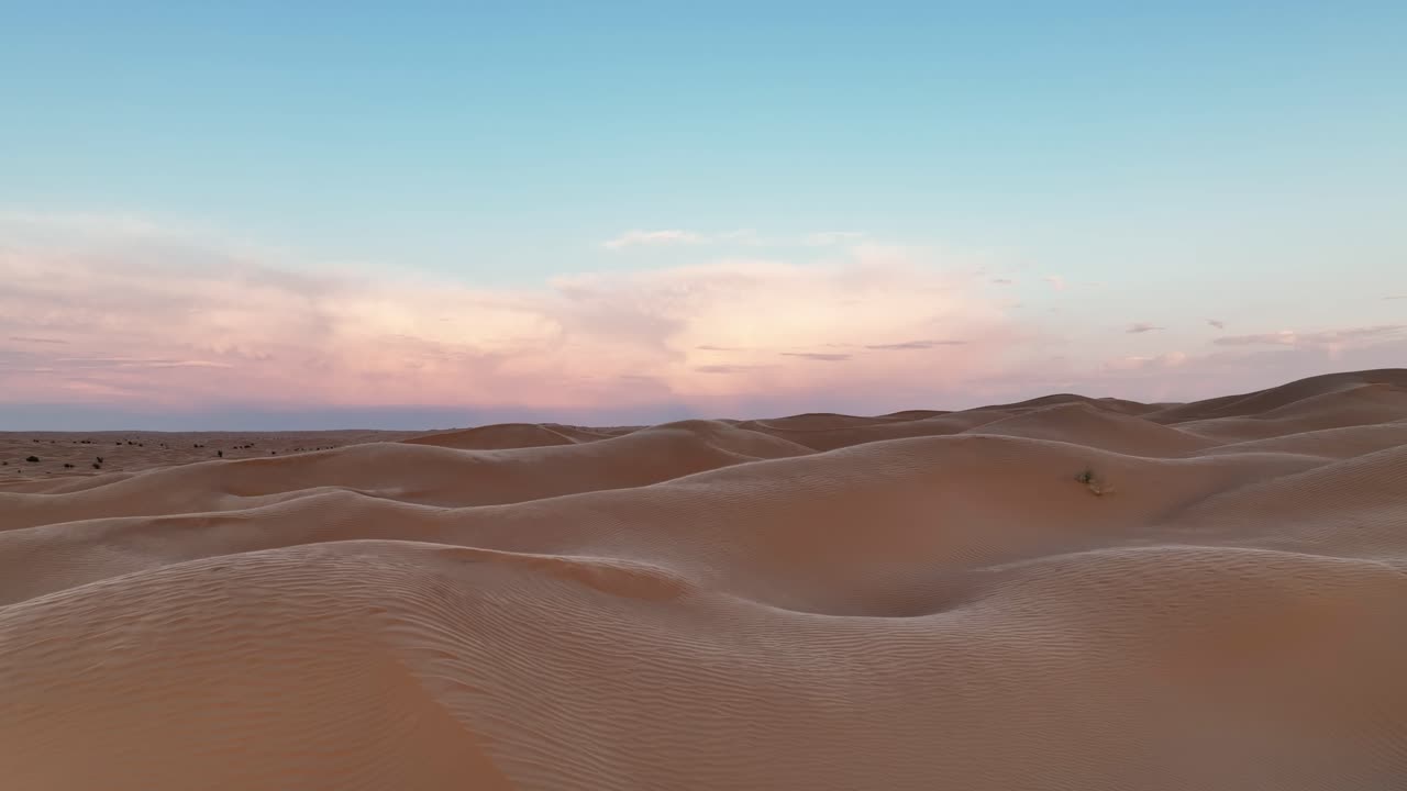 дрон летит низко над дюнами пустыни сахара с ветром, дующим песком над дюнами с восходящим солнцем в тунисе.