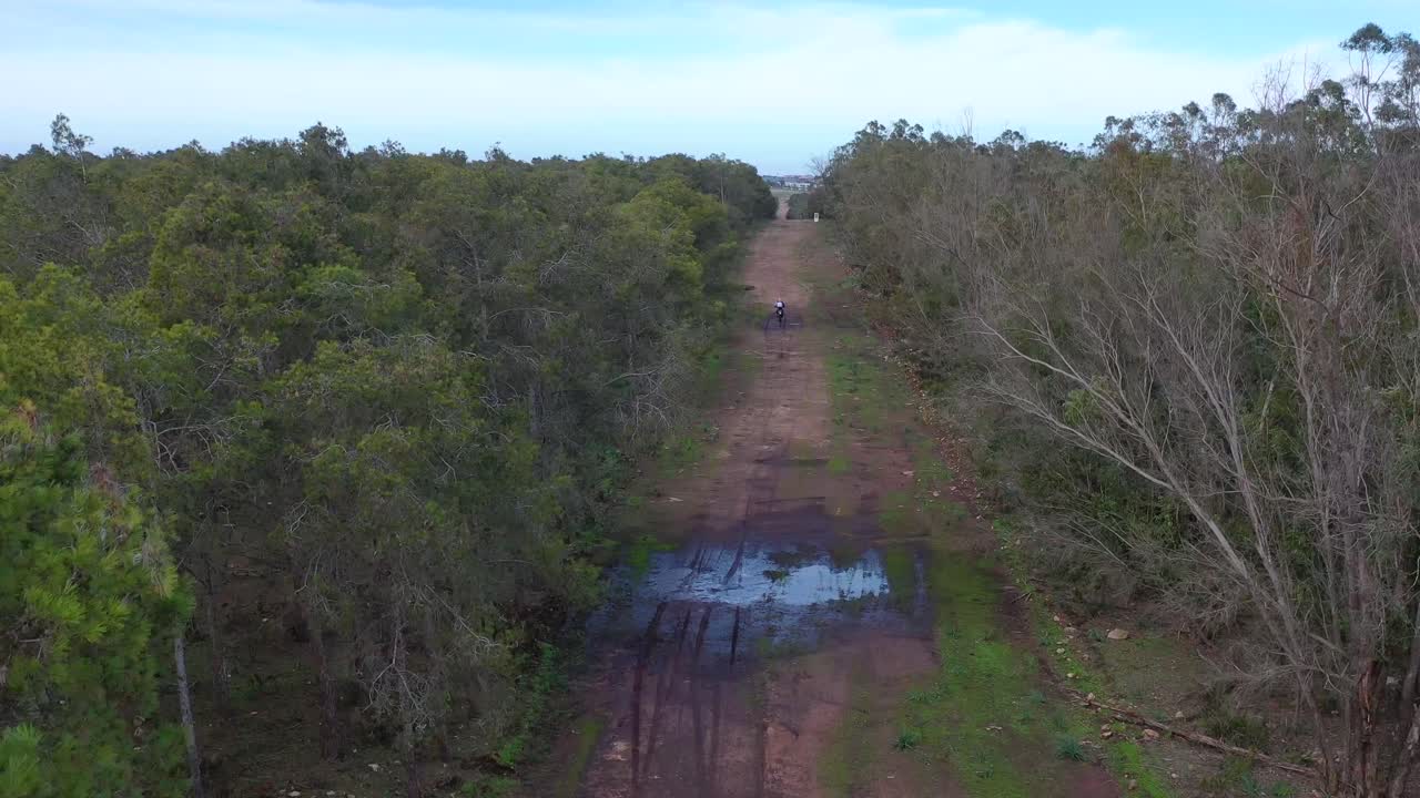 먼지 자전거 오토바이 라이더는 큰 물 웅덩이가 있는 뒷길 지역에서 운전합니다.