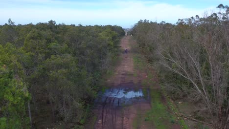 A-Dirt-Bike-Motorcycle-Rider-Drives-On-A-Backroad-Area-With-Some-Large-Water-Puddles