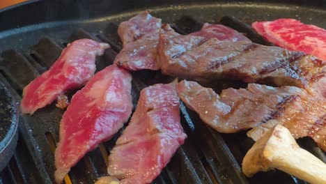 hand uses tongs to turn juicy marbled beef slices while grilling on a hot korean bbq tabletop grill