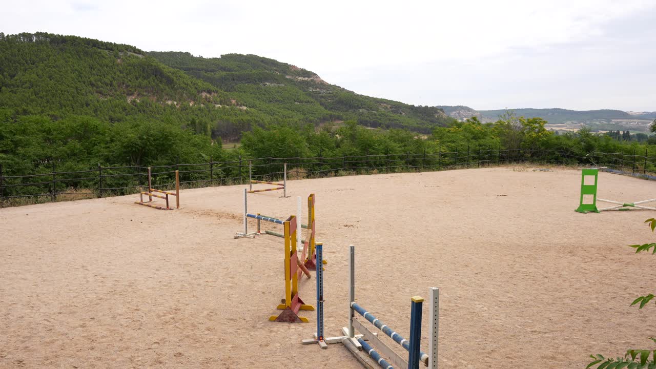 Panning left over a competition horse track with multiple hurdles amid green vegetation, 4K