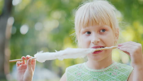 la niña está terminando los restos de un delicioso algodón dulce se sienta en el parque en un ingenio video banco